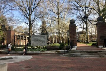 A woman wearing a cap and gown poses for a photo in front of tulips at the campus of Ohio University in Athens, Ohio, USA on April 21, 2022 as graduation nears.