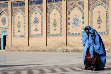 Two women in blue burqas walk at the front of a mosque with a door open, symbolising an open university