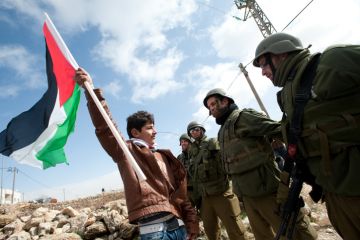 Al-Masara, Occupied Palestinian Territories - January 27, 2012 A Palestinian youth waves a flag while confronting Israeli soldiers in a protest against the Israeli separation barrier in the West Bank down of Al-Masara.