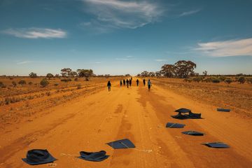 People walk down a dusty outback road, their abandoned mortar boards behind them
