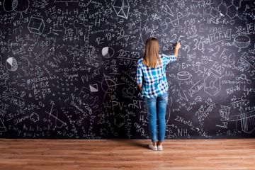 A woman writing on a blackboard that is covered in writing