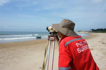 Binh Thuan, Viet Nam - October 21, 2014 Asian engineer work on Vietnamese beach, man looking in theodolite to survey sea level, measurement device set on tripod, Vietnam, Oct 21, 2013 Binh Thuan, Viet Nam - October 21, 2014 Asian engineer work on Vietnamese beach, man looking in theodolite to survey sea level, measurement device set on tripod, Vietnam, Oct 21, 2013