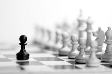 Black chess pawn in front of full set of white pieces