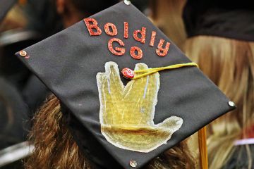 A mortarboard with 'Boldly Go' written on it during a graduation ceremony. To illustrate a new higher education provider that is offering master’s programmes taught by artificial intelligence.