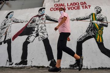 A woman passes by graffiti depicting Brazilian President Jair Bolsonaro pulling a rope against health workers with the question "Which side of the rope are you on?", Brazil, 2020. To illustrate ‘political shocks’ hitting women’s representation in science.