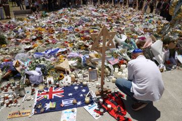 A mourner lights candles as people gather around floral tributes outside Bondi Pavilion in Sydney on 17 December, 2025, to honour victims of the Bondi Beach shooting.