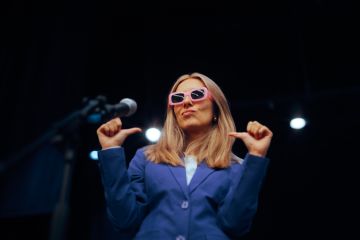 A woman in pink glases points to herself, illustrating showing off on socail media A woman in pink glases points to herself, illustrating showing off on socail media