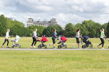 Women push children’s buggies across a park