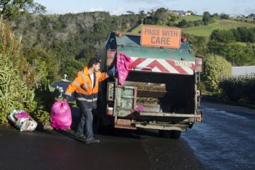 Cable Bay, New Zealand - July 25, 2013 Waste management worker throws rubbish into a rubbish truck on the side of the road