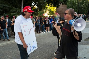 A man holds a sign that says "For Charlie" as people protest outside the "American Comeback Tour" event at Northrop Auditorium on the University of Minnesota campus on 22 September, 2025. The event was held after the assassination of Charlie Kirk.