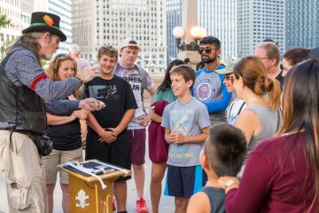 Chicago, IL, August 17, 2017 Downtown Chicago, a street performer magician entertains tourist families. Chicago attracts millions of visitors each year. Chicago, IL, August 17, 2017 Downtown Chicago, a street performer magician entertains tourist families. Chicago attracts millions of visitors each year.
