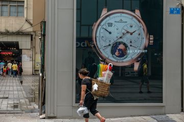 A local woman carries a bamboo basket, walking past a luxury watch shop at Jiefangbei CBD, Chongqing, 2015 A local woman carries a bamboo basket, walking past a luxury watch shop at Jiefangbei CBD, Chongqing, 2015