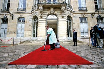 A woman vacuums a red carpet outside a posh building A woman vacuums a red carpet outside a posh building