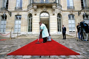 A woman vacuums a red carpet outside a posh building