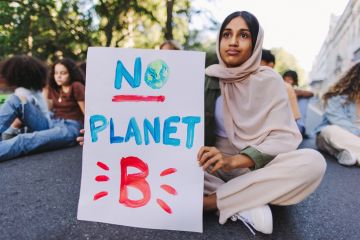 A climate protester sits in the road with "no planet B" sign