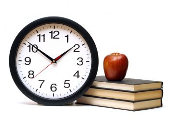 Clocks next to pile of books with apple