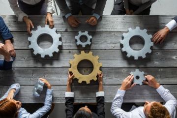 People hold unconnected cogwheels, one of which is gold People hold unconnected cogwheels, one of which is gold