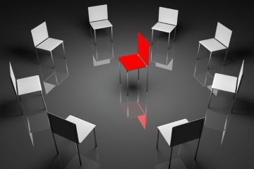 A circle of grey chairs with one red chair in the centre