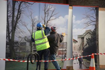 Construction workers installing hoarding around a property development site, to illustrate that universities must choose between physical or digital development.
