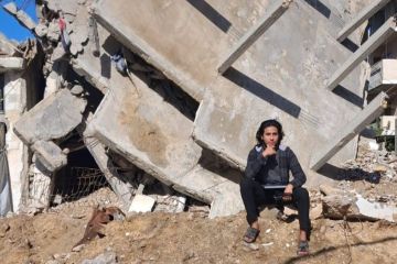 A young student in Gaza sitting near the ruins of his home