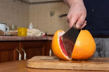 Cutting a grapefruit with a kitchen hatchet on a wood board