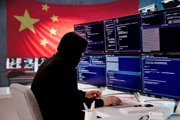 Cybersecurity expert coding with Chinese flag displayed In background. To illustrate that universities have been told by MI5 to review their ties with a Chinese research institute after spy warning. Cybersecurity expert coding with Chinese flag displayed In background. To illustrate that universities have been told by MI5 to review their ties with a Chinese research institute after spy warning.