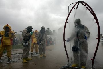 A person in a chemical protection suit walks through a decontamination shower as another is washed down during a mock chemical attack. To illustrate researchers might need to demand retraction of their own papers to decontaminate scientific literature.