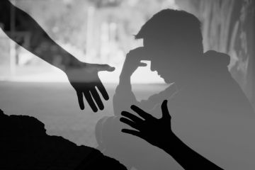 Hands reach for each other in front of a depressed man, symbolising suicide prevention Hands reach for each other in front of a depressed man, symbolising suicide prevention