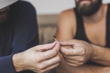Detail of two men sitting on a couch, sharing a joint, smoking pot