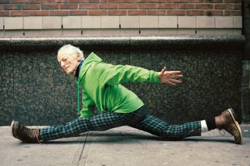 Elderly man doing spilts on street pavement