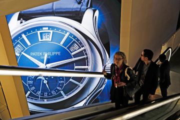 Visitors traveling on an escalator pass a Patek Philippe luxury wristwatch advertisement. To illustrate that there has been an increase in the number of staff paid more than £100,000 at Russell Group universities.