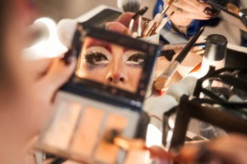 A drag queen applies make-up looking in a hand-mirror Face of drag queen