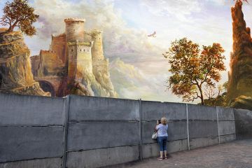 A woman peeks through a grey wall to a magnificent castle on the other side