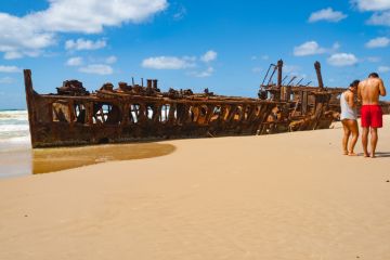 Fraser Island Australia; Two tourists on beach by Maheno shipwreck rusting away on beach Fraser Island Australia; Two tourists on beach by Maheno shipwreck rusting away on beach