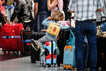 Travellers sit on their suitcases at the check-in counters