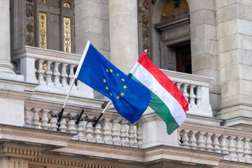 Flags of the European Union and Hungary flying from poles outside an ornate building in the centre of Budapest