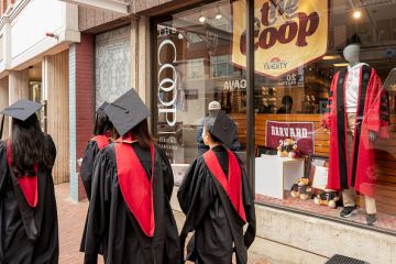 Harvard University students wearing graduation gowns walk past a bookstore near the Harvard University campus in Cambridge, Massachusetts, US