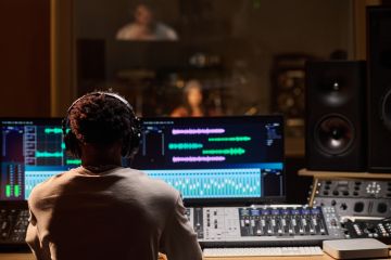 Young Adult Man Wearing Headphones Monitoring Audio Levels in Studio Young Adult Man Wearing Headphones Monitoring Audio Levels in Studio