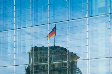 A reflection of the german flag on top of the Reichstag building on a glass facade