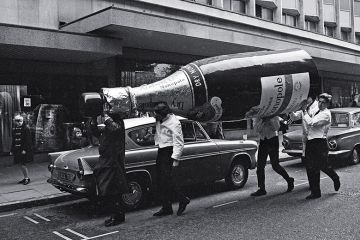 A giant champagne bottle outside the department store Rackhams, Birmingham, UK, 1966. To illustrate high pay for leaders of private UK providers.