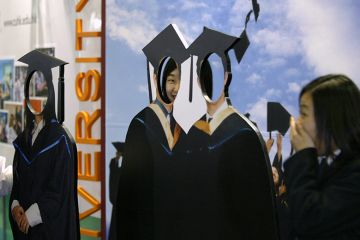 Visitors to a careers expo peek through a cardboard cut out of graduates. To illustrate 'fake' students which can be pushed by recruitment agents.