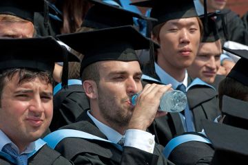 A graduation ceremony with a graduate drinking water and looking hot, UK. To illustrate that dealing with extreme heat is ‘hugely problematic’ for universities.