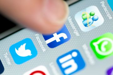 Hand tapping social media icon on smartphone screen