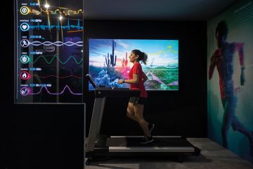 A woman runs on a running machine while some health stats are foregrounded A woman runs on a running machine while some health stats are foregrounded