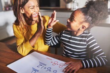 A woman high fives her daughter while she does her homework A woman high fives her daughter while she does her homework