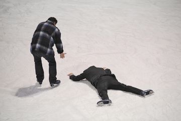 Man helps fellow skater who has fallen on the ice