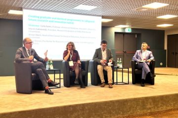Four panelists sitting on couches on a stage in front of a screen at the THE Europe summit