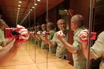 Man taking selfie of reflections in infinity mirror, illustrating tedium when conferences are dominated by authors with multiple papers. 