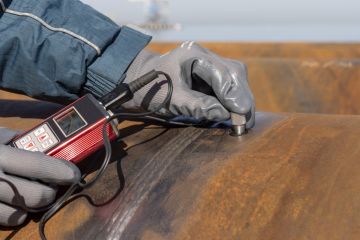 Inspector is measuring thickness of the pipe material from near to weld with a portable ultrasonic wall thickness measurement gauge. It is a method of performing non destructive measurement (gauging)