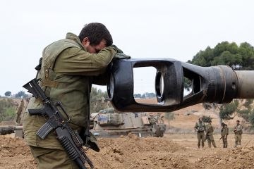 An Israeli soldier rests his head on the gun barrel of a self-propelled artillery howitzer as Israeli soldiers take positions near the border with Gaza in southern Israel on October 9, 2023